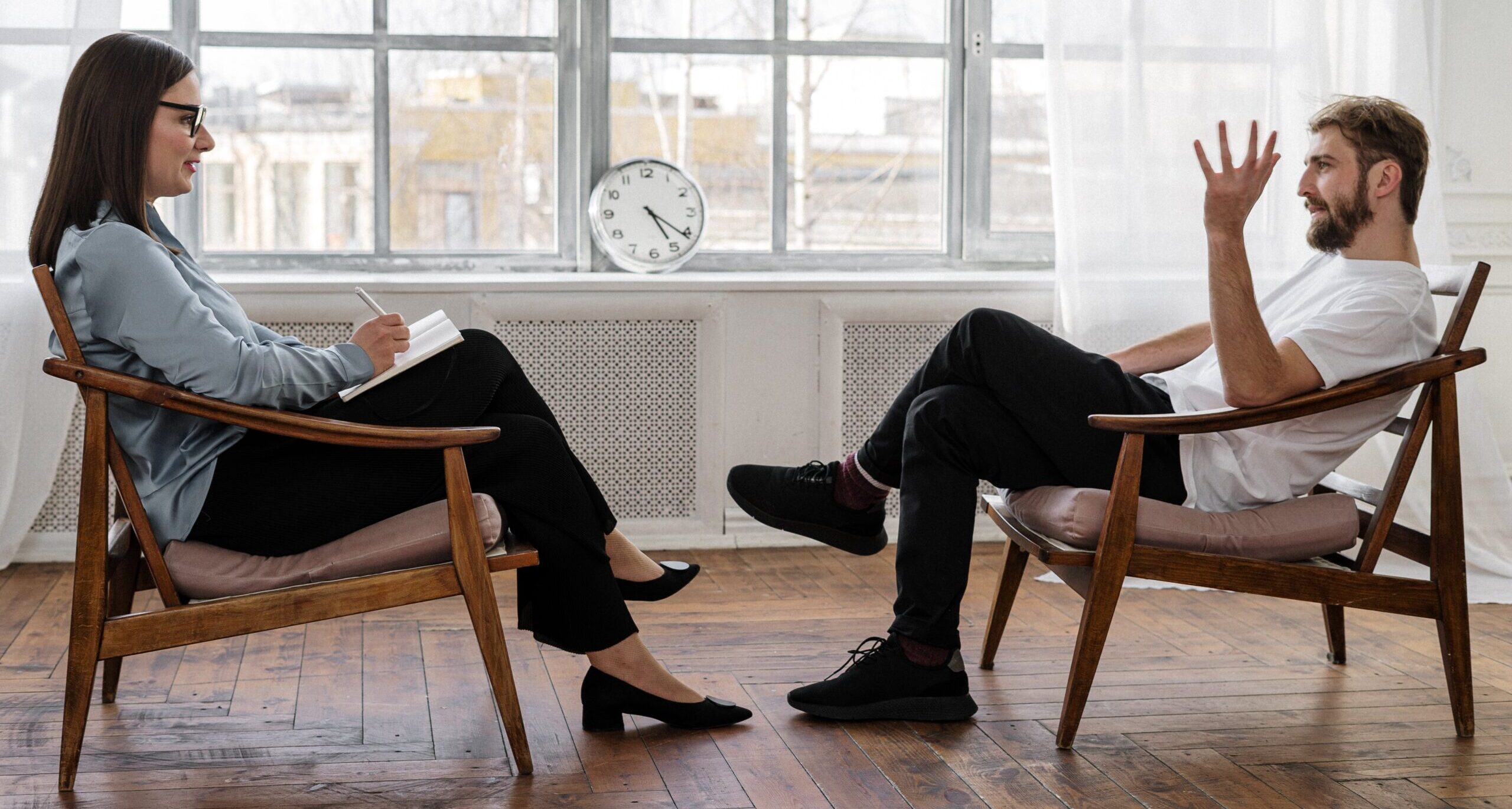 Person in Black Pants and Black Shoes Sitting on Brown Wooden Chair